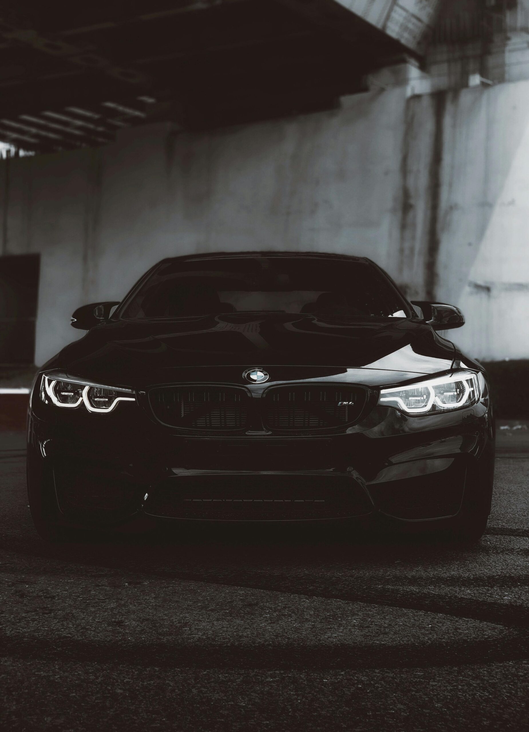 Front view of a black BMW M4 car parked under dim lighting for a bold and stylish appearance.
