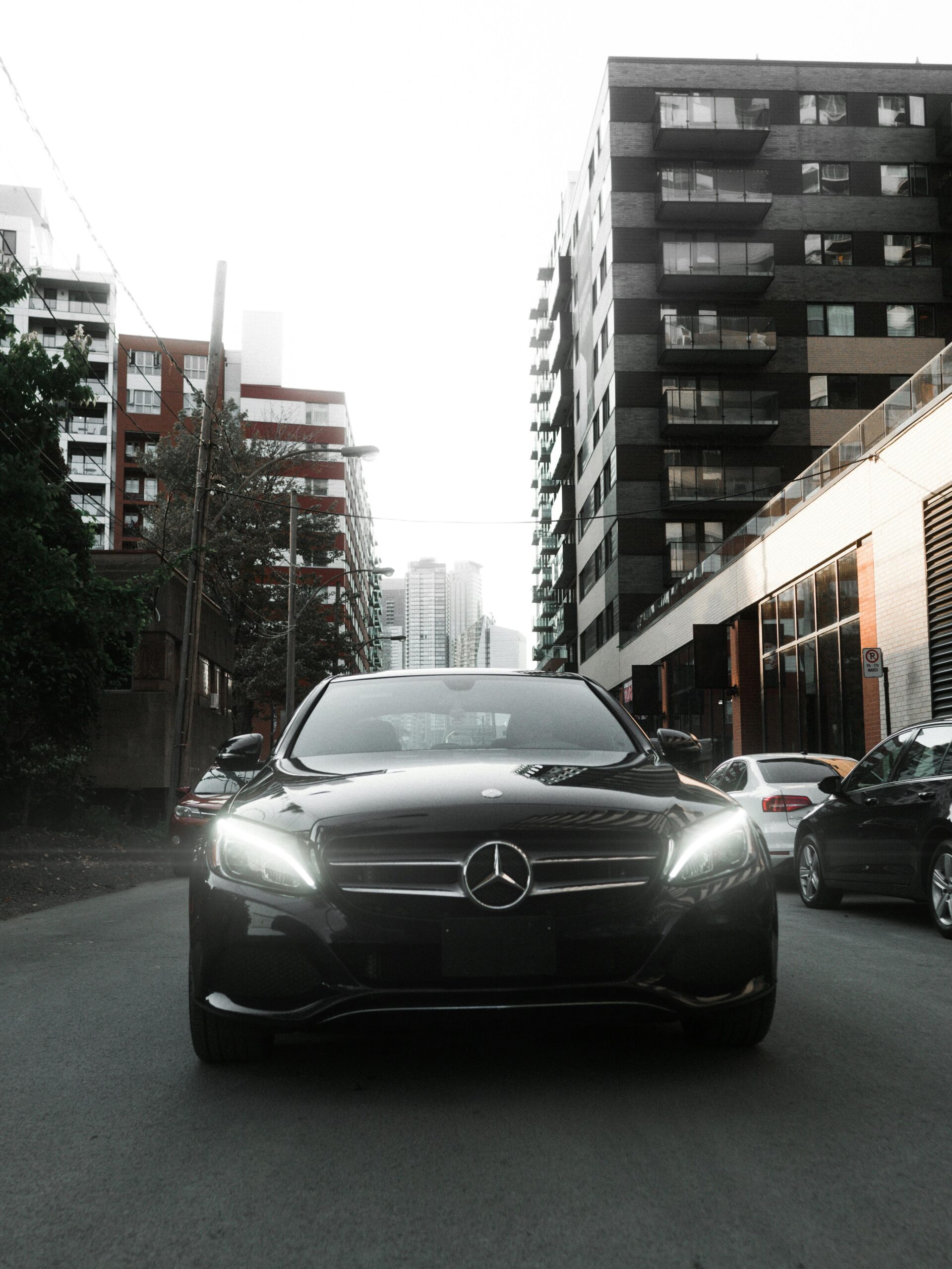 Front view of a sleek black Mercedes amidst city buildings, exuding luxury and class.