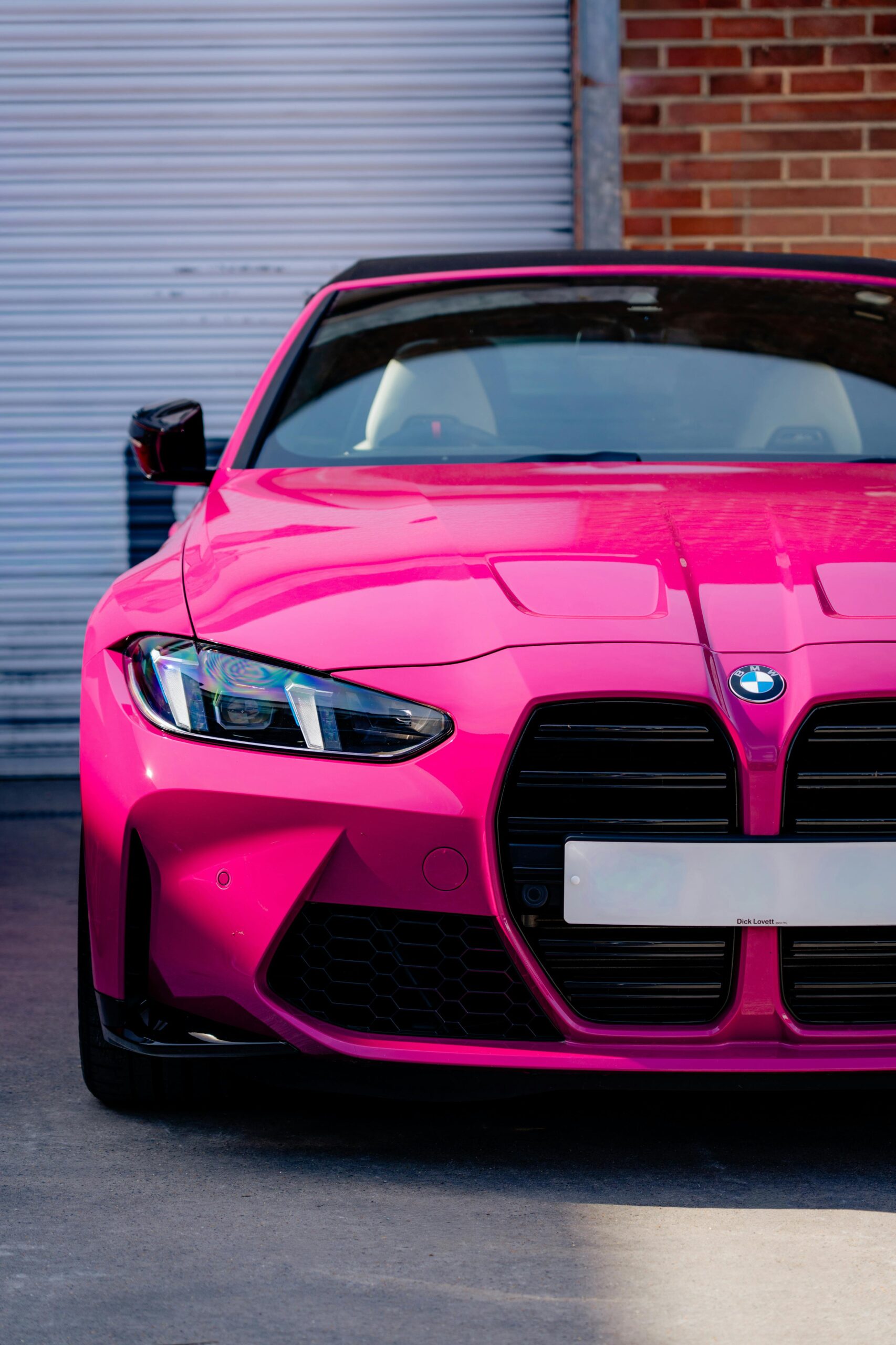 A striking pink car parked outdoors against a brick and metal backdrop, emphasizing modern automotive design.